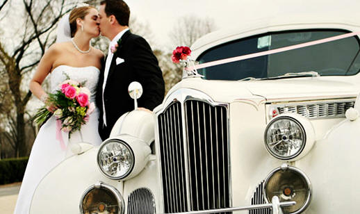 Bride and groom kissing beside a vintage white car